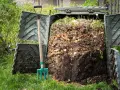 Widok na otwarty kompostownik z widocznymi resztkami organicznymi i widłami obok. To praktyczny sposób, jak zrobić kompostownik.