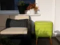 Zielony kompostownik na balkonie, obok wygodnej kanapy z poduszką w grochy.