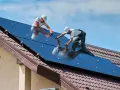 Dwóch mężczyzn montuje panele fotowoltaiczne na dachu. To przyszłość energetyki w Polsce.