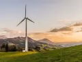 Wiatrak na zielonym wzgórzu, symbolizujący czystą energię z wiatru, na tle malowniczych gór o zachodzie słońca.
