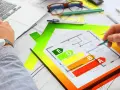 Rysunek domu z klasyfikacją energetyczną od A do E. Inżynier analizuje projekt, przygotowując świadectwo energetyczne.