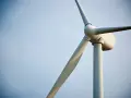 Biały wiatrak elektrownia na tle błękitnego nieba. Jego łopaty obracają się, czerpiąc energię z wiatru.