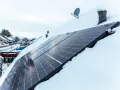Panele fotowoltaiczne na dachu pokrytym śniegiem. Nawet zimą, przy odpowiednim nachyleniu, mogą produkować energię.
