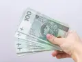 Dłoń trzyma stos banknotów 100 zł. Czy to zapowiedź bonu energetycznego dla każdego?
