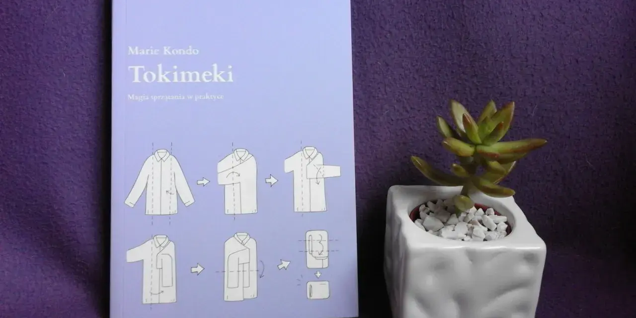 Książka "Tokimeki" Marie Kondo z instrukcją składania ubrań. Odkryj magię sprzątania i porządek w szafie. Obok mała roślinka w doniczce.