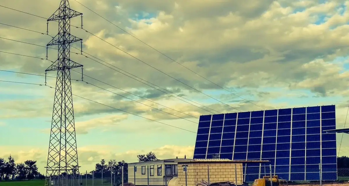 Własny prąd bez podłączenia do sieci: duża farma fotowoltaiczna obok wieży energetycznej i przyczepy mieszkalnej.