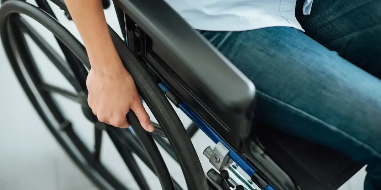 Osoba na wózku trzymająca koło. Ulga na prąd dla niepełnosprawnych Tauron to wsparcie dla osób potrzebujących.
