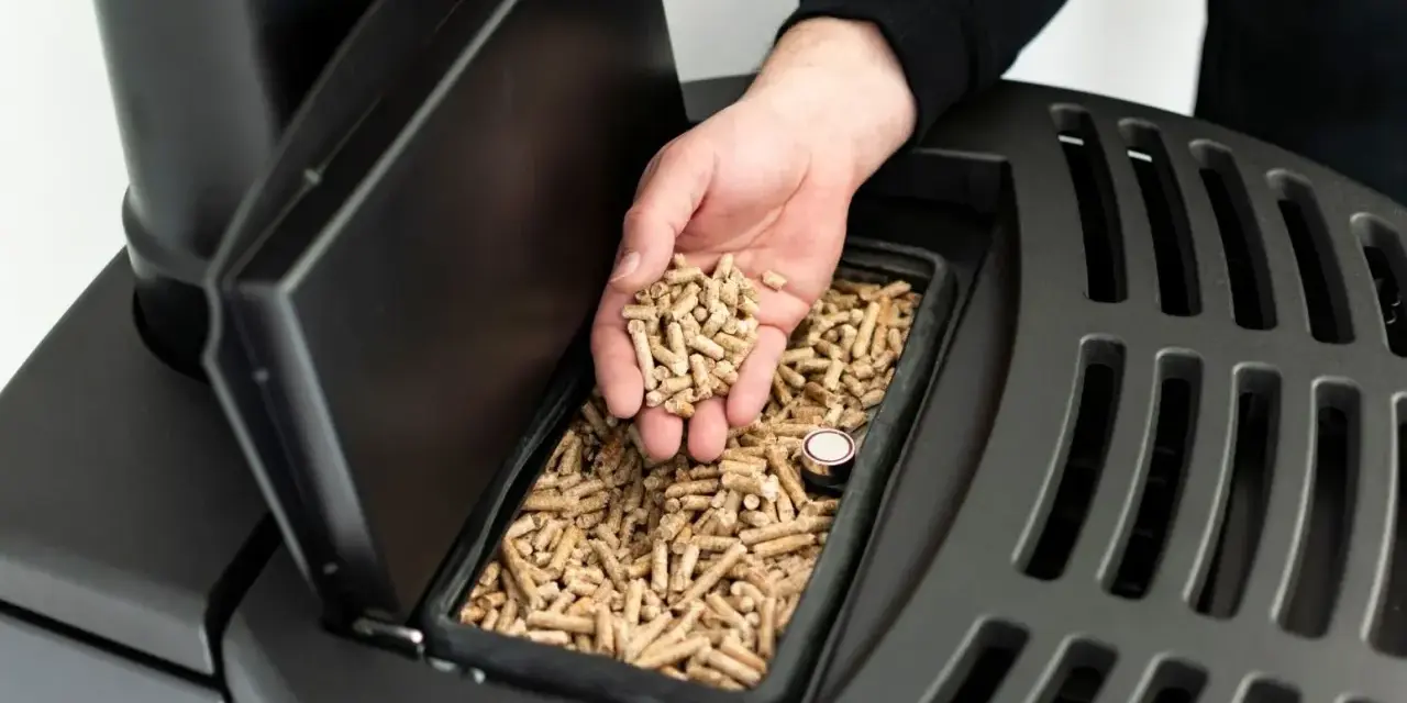 Dłoń wsypuje pellet do czarnego pieca. Czy piec na pellet można odliczyć od podatku? Dowiedz się więcej o ekologicznym ogrzewaniu.