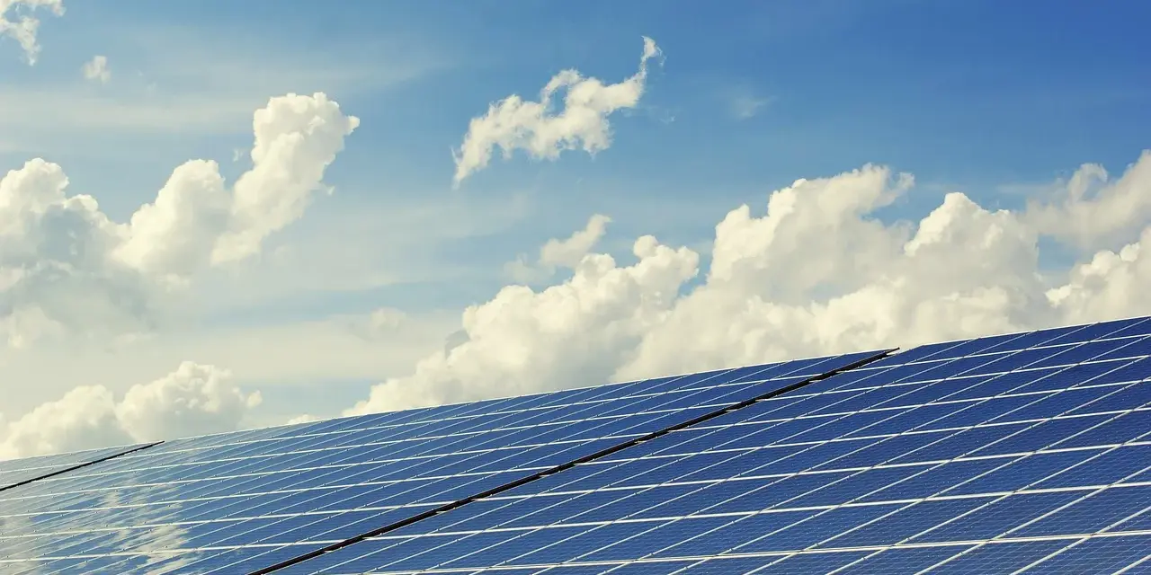 Panele słoneczne na tle błękitnego nieba z chmurami. To dowód na liczne zalety energii słonecznej – czystej i odnawialnej.