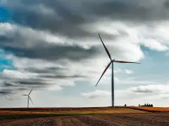 Imponująca wysokość wiatraków na tle burzowego nieba. Dwa wiatraki dominują krajobraz, jeden bliżej, drugi dalej.