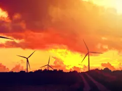Zachód słońca nad farmą wiatrową. Płonące chmury tworzą energetyczny spektakl, a wiatraki wirują, czerpiąc siłę z natury.