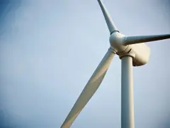 Biały wiatrak elektrownia na tle błękitnego nieba. Jego łopaty obracają się, czerpiąc energię z wiatru.