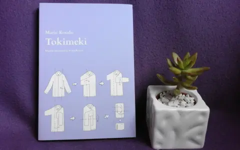 Książka "Tokimeki" Marie Kondo z instrukcją składania ubrań. Odkryj magię sprzątania i porządek w szafie. Obok mała roślinka w doniczce.