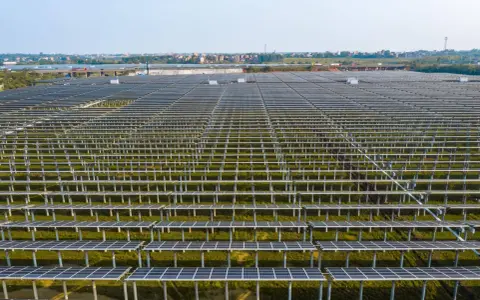 Ogromne połacie paneli fotowoltaicznych, część rozbudowy instalacji Tauron, na tle miejskiej zabudowy.