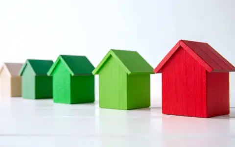 Rząd domków: beżowy, zielony, zielony, zielony, czerwony. Symbolizują różne poziomy klasy energetycznej.