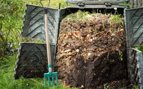Widok na otwarty kompostownik z widocznymi resztkami organicznymi i widłami obok. To praktyczny sposób, jak zrobić kompostownik.
