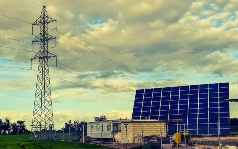 Własny prąd bez podłączenia do sieci: duża farma fotowoltaiczna obok wieży energetycznej i przyczepy mieszkalnej.