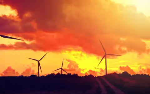 Zachód słońca nad farmą wiatrową. Płonące chmury tworzą energetyczny spektakl, a wiatraki wirują, czerpiąc siłę z natury.
