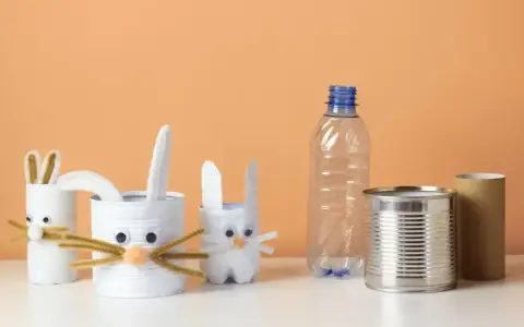 Zające z rolek po papierze i puszek to świetne przykłady recyklingu w życiu codziennym. W tle pusta butelka i rolka po ręczniku papierowym.