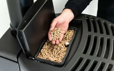 Dłoń wsypuje pellet do czarnego pieca. Czy piec na pellet można odliczyć od podatku? Dowiedz się więcej o ekologicznym ogrzewaniu.