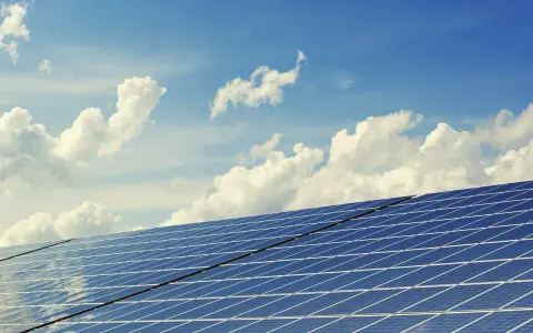 Panele słoneczne na tle błękitnego nieba z chmurami. To dowód na liczne zalety energii słonecznej – czystej i odnawialnej.