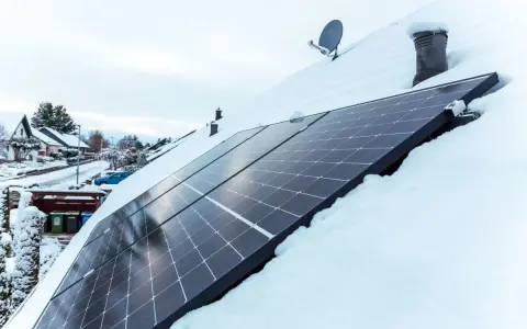 Panele fotowoltaiczne na dachu pokrytym śniegiem. Nawet zimą, przy odpowiednim nachyleniu, mogą produkować energię.