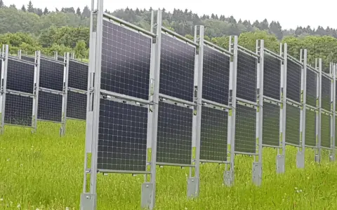Rzędy wydajnych paneli fotowoltaicznych na tle zielonego lasu. Instalacja na łące, gotowa do produkcji czystej energii.