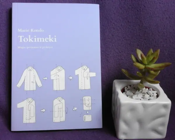 Książka "Tokimeki" Marie Kondo z instrukcją składania ubrań. Odkryj magię sprzątania i porządek w szafie. Obok mała roślinka w doniczce.