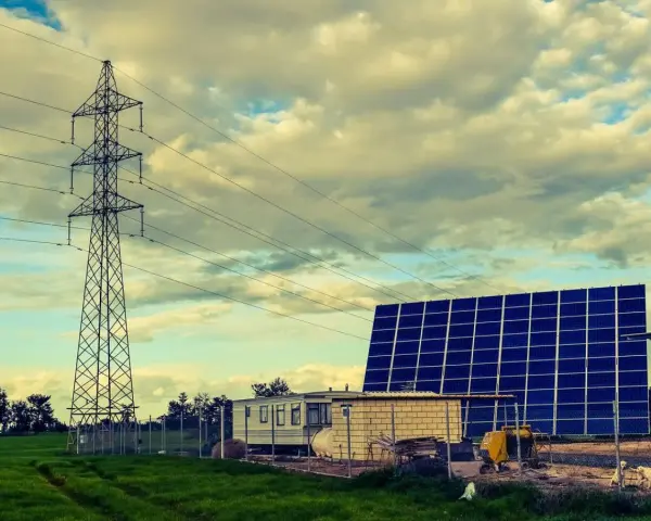 Własny prąd bez podłączenia do sieci: duża farma fotowoltaiczna obok wieży energetycznej i przyczepy mieszkalnej.