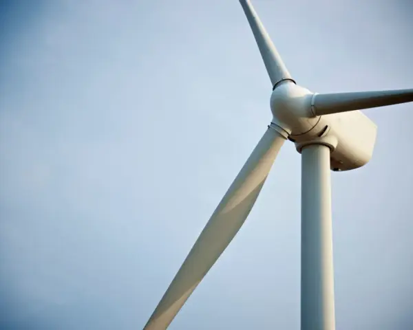 Biały wiatrak elektrownia na tle błękitnego nieba. Jego łopaty obracają się, czerpiąc energię z wiatru.
