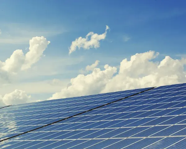 Panele słoneczne na tle błękitnego nieba z chmurami. To dowód na liczne zalety energii słonecznej – czystej i odnawialnej.