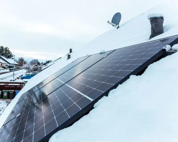 Panele fotowoltaiczne na dachu pokrytym śniegiem. Nawet zimą, przy odpowiednim nachyleniu, mogą produkować energię.