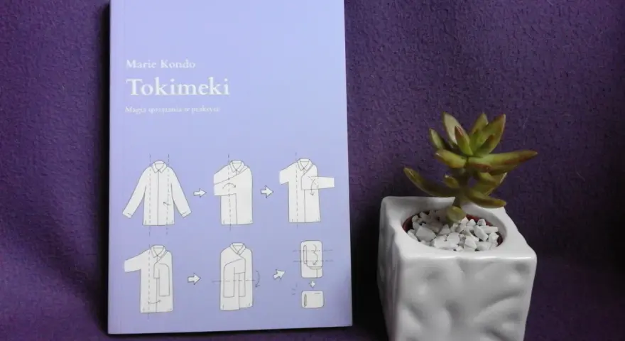 Książka "Tokimeki" Marie Kondo z instrukcją składania ubrań. Odkryj magię sprzątania i porządek w szafie. Obok mała roślinka w doniczce.