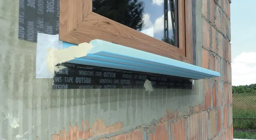 Fragment okna w trakcie ciepłego montażu. Widoczna taśma uszczelniająca i izolacja pod parapetem.