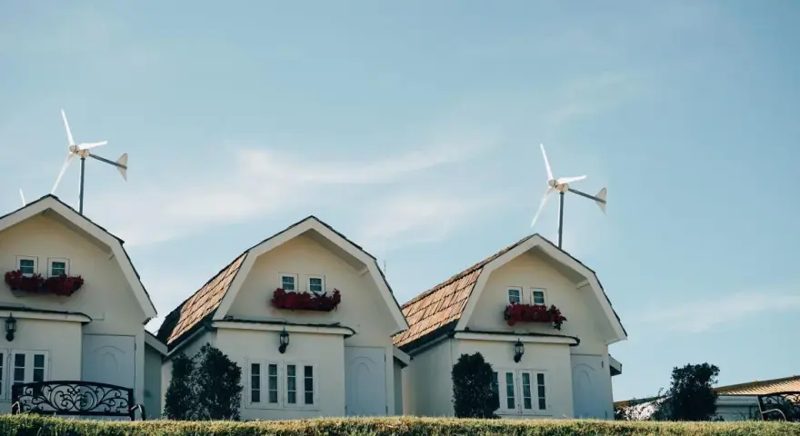 Domy z czerwonymi kwiatami i turbina wiatrowa bez pozwolenia na dachu.