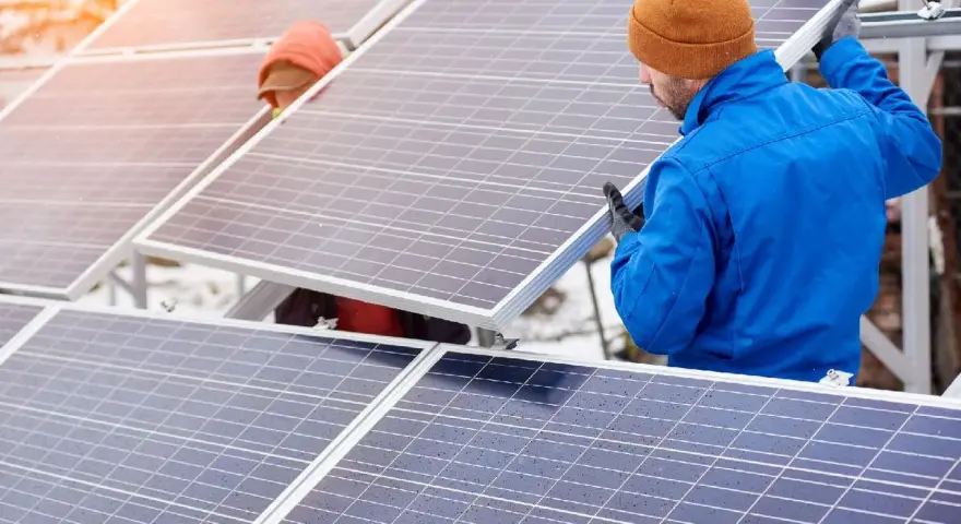 Pracownicy montują panele fotowoltaiczne. W tle widać śnieg i słońce. Utylizacja paneli fotowoltaicznych to ważny etap cyklu życia instalacji.