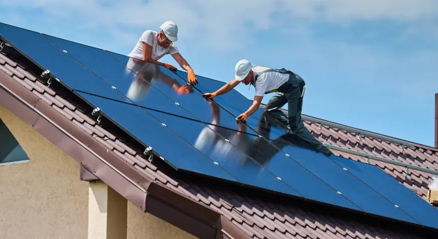Dwóch mężczyzn montuje panele fotowoltaiczne na dachu. To przyszłość energetyki w Polsce.