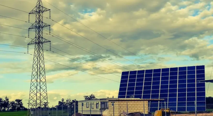Własny prąd bez podłączenia do sieci: duża farma fotowoltaiczna obok wieży energetycznej i przyczepy mieszkalnej.
