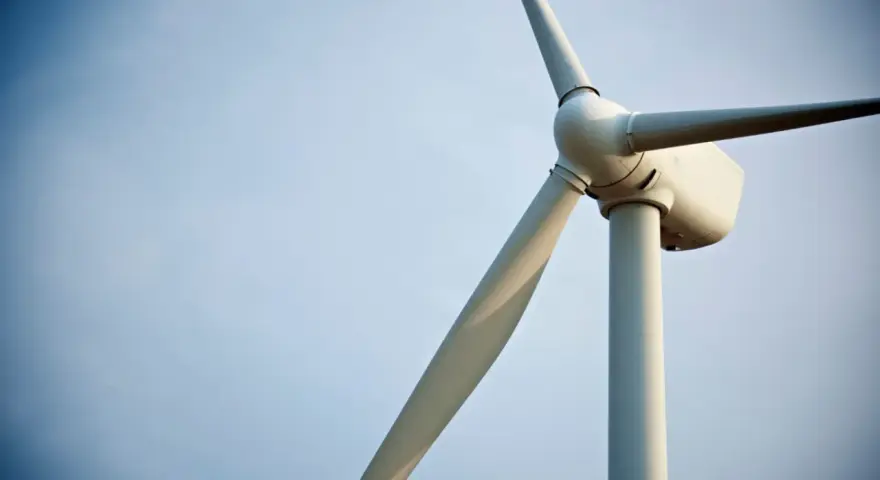 Biały wiatrak elektrownia na tle błękitnego nieba. Jego łopaty obracają się, czerpiąc energię z wiatru.