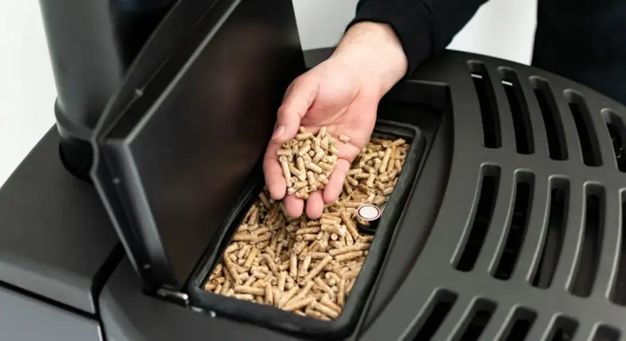 Dłoń wsypuje pellet do czarnego pieca. Czy piec na pellet można odliczyć od podatku? Dowiedz się więcej o ekologicznym ogrzewaniu.