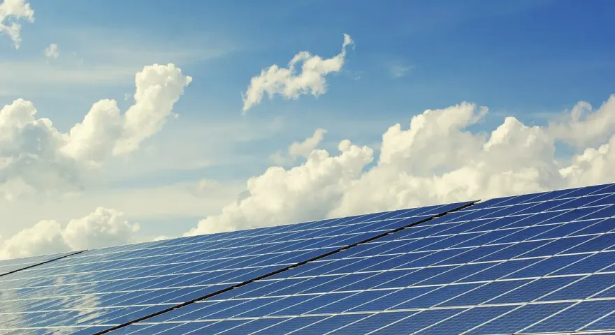 Panele słoneczne na tle błękitnego nieba z chmurami. To dowód na liczne zalety energii słonecznej – czystej i odnawialnej.