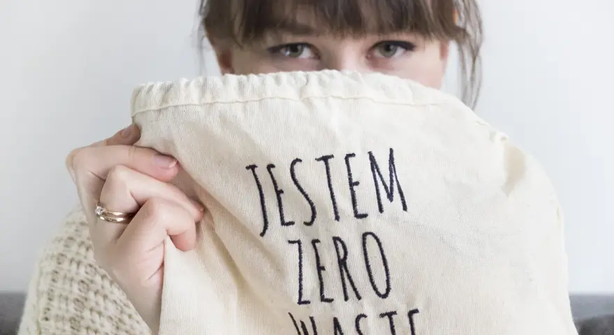 Sylwia Majcher, z uśmiechem ukrytym za torbą z napisem "Jestem Zero Waste", pokazuje swoje zaangażowanie w ekologię.