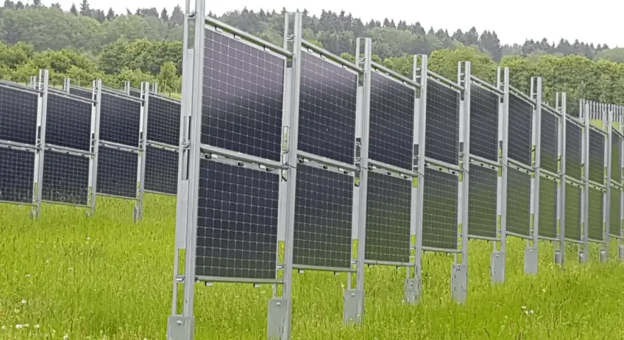 Rzędy wydajnych paneli fotowoltaicznych na tle zielonego lasu. Instalacja na łące, gotowa do produkcji czystej energii.