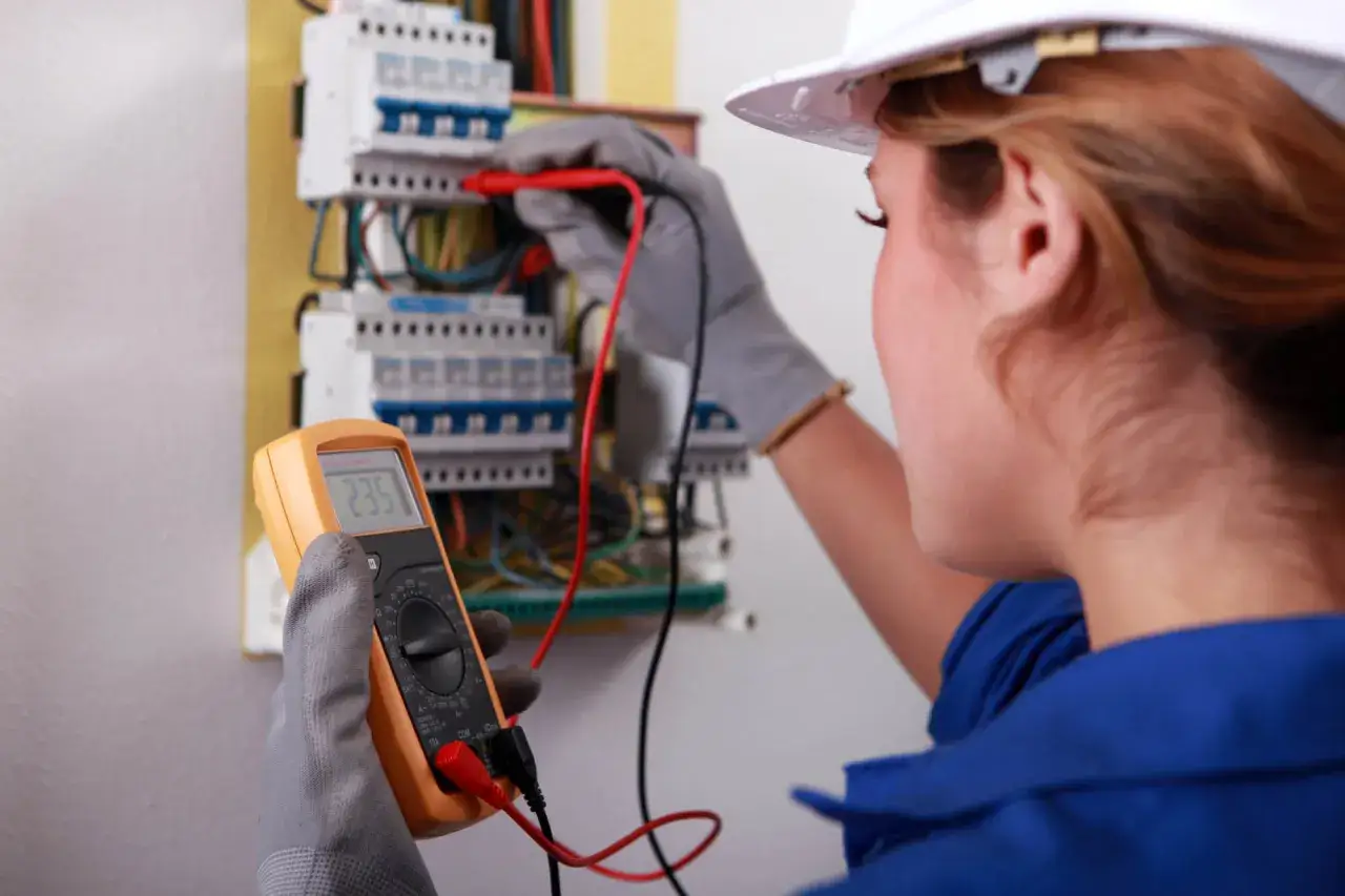 Elektryk wykonuje protokół pomiarów elektrycznych domu jednorodzinnego, używając multimetru do sprawdzenia napięcia.