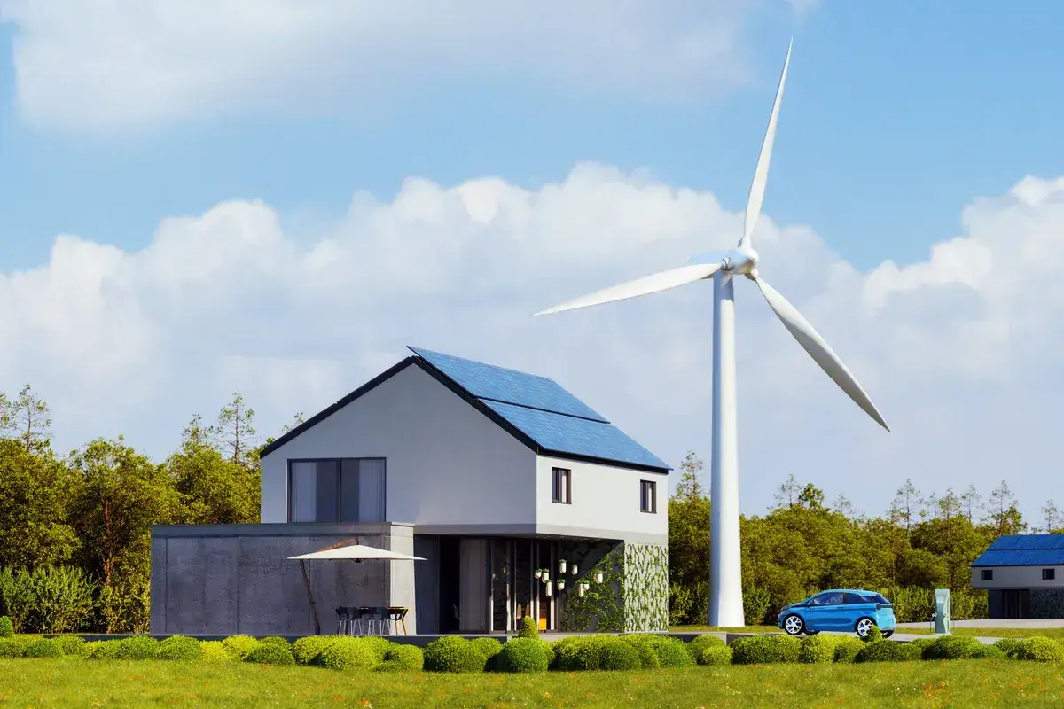 Nowoczesny dom z panelami słonecznymi i mała elektrownia wiatrowa w tle. Obok stoi niebieski samochód elektryczny.