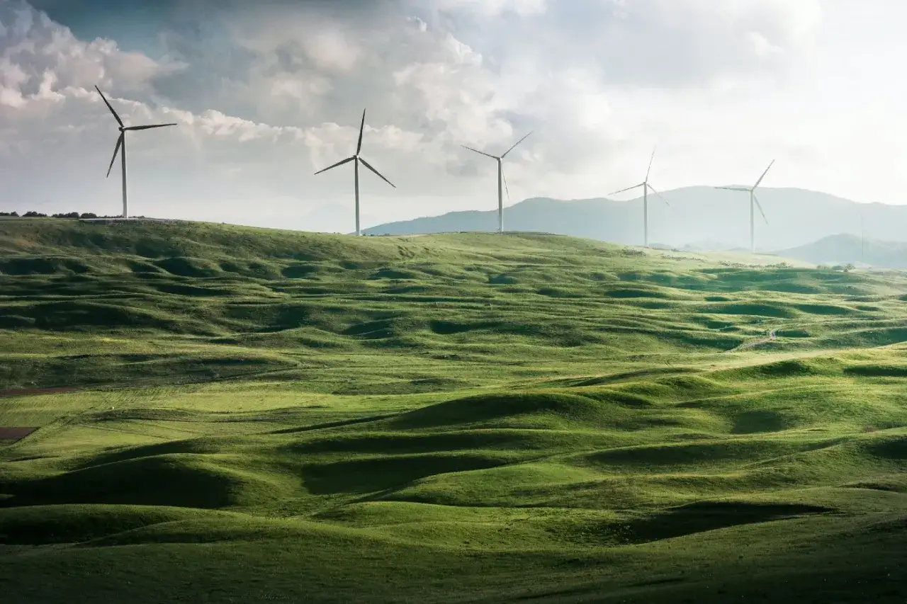Zielone wzg&oacute;rza i wiatraki na horyzoncie symbolizują zalety elektrowni wiatrowej: czystą energię dla przyszłości.