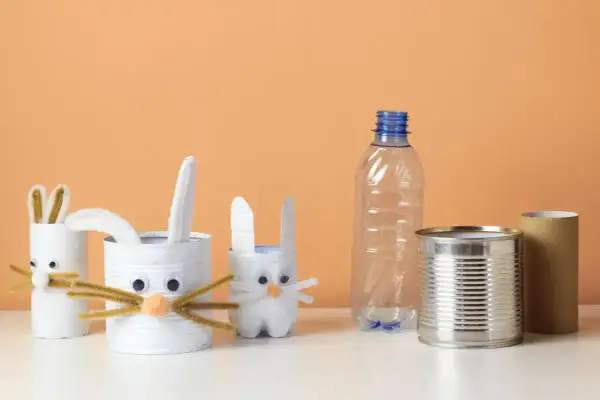 Zające z rolek po papierze i puszek to świetne przykłady recyklingu w życiu codziennym. W tle pusta butelka i rolka po ręczniku papierowym.